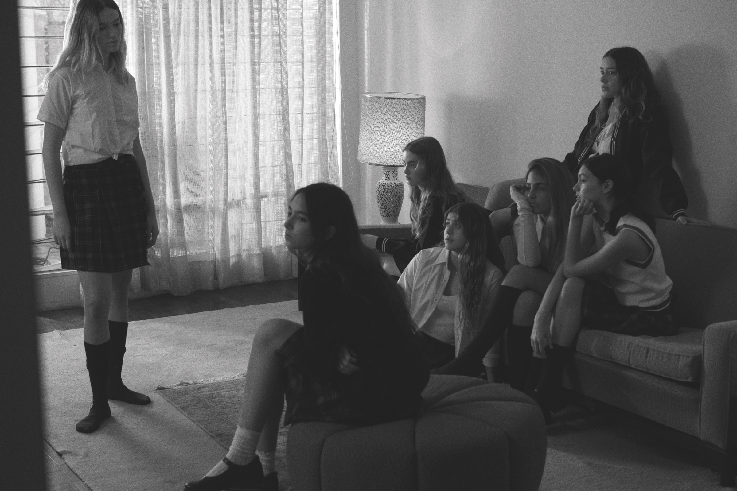 A group of young people gathered in a living room, photographed in black and white.