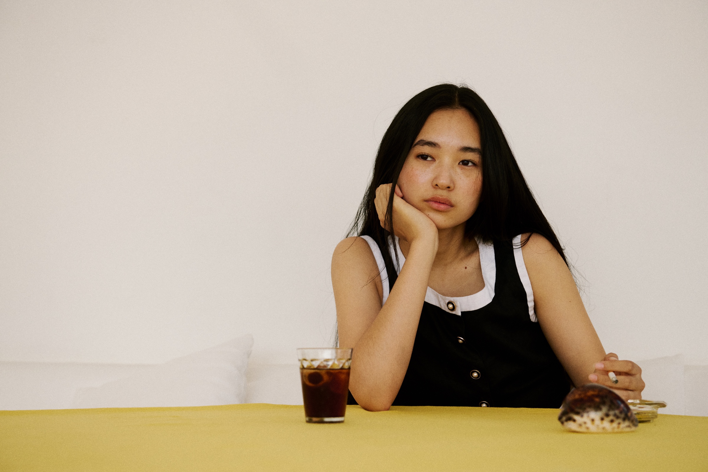 A seated young woman looks away across a yellow table.
