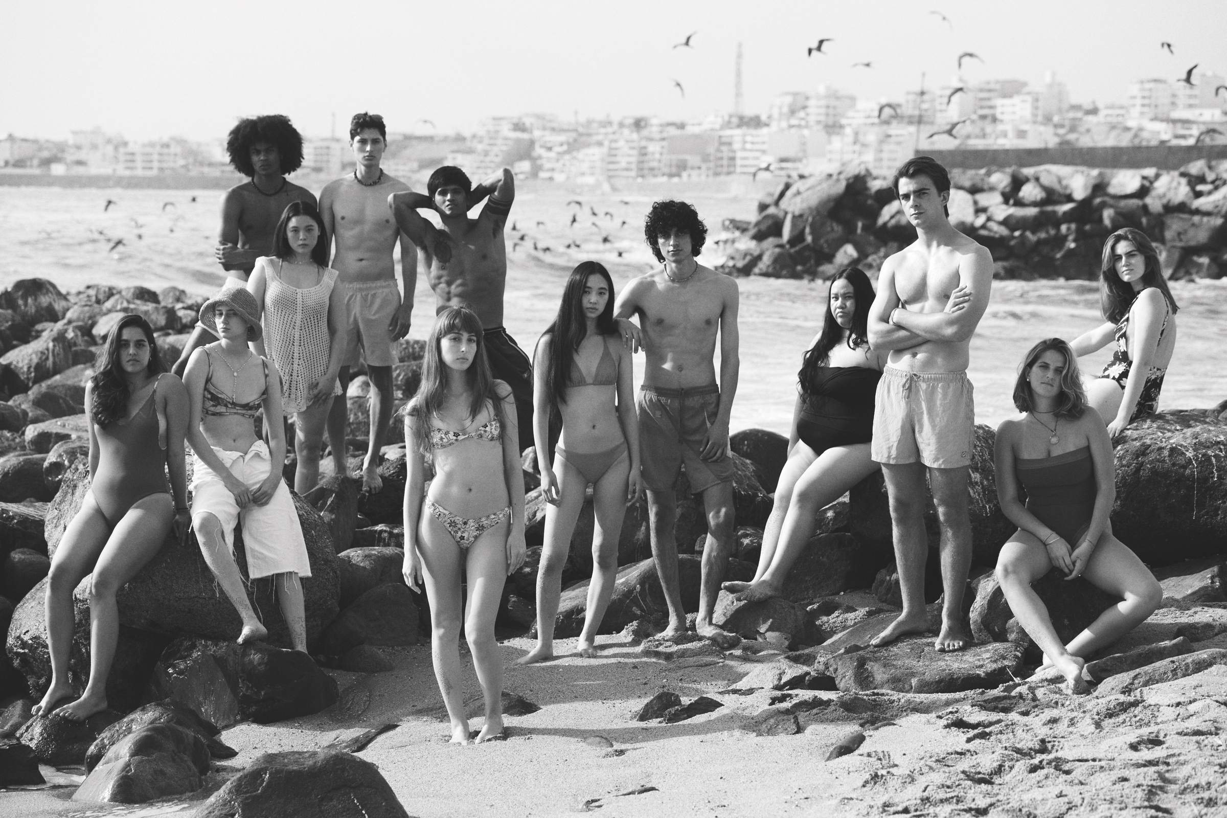 A group of young people poses on rocks beside the sea.