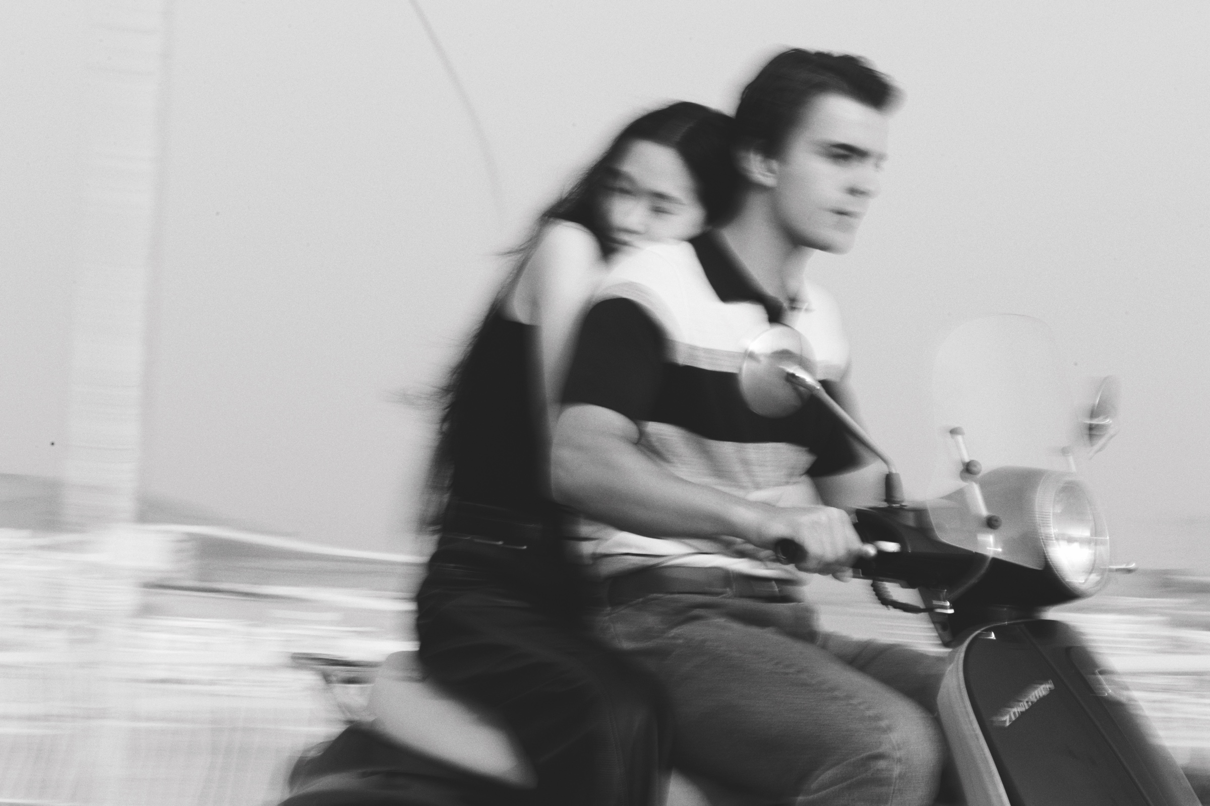 Two young people ride a scooter, blurred in motion.