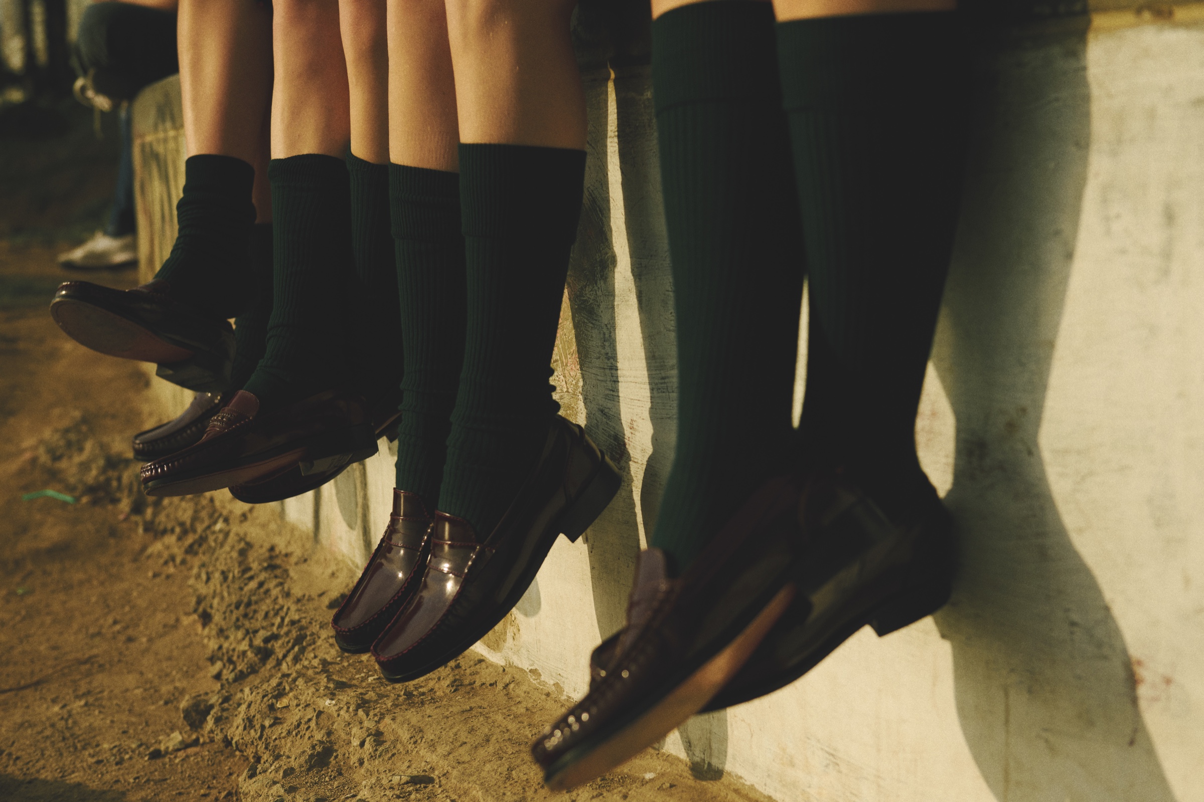 A row of students’ legs in green socks and brown shoes.
