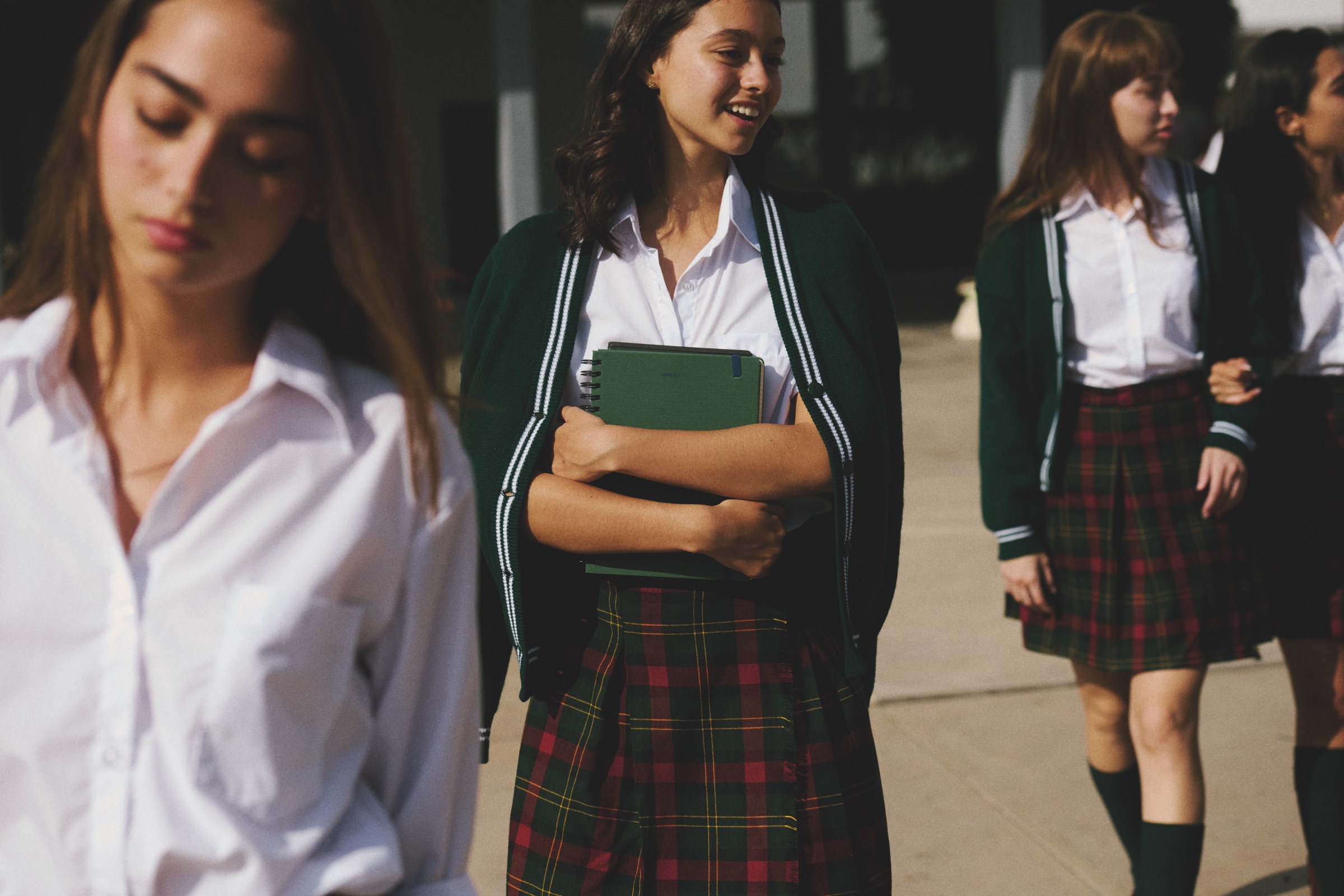 Students in green cardigans and plaid uniforms stand outside.