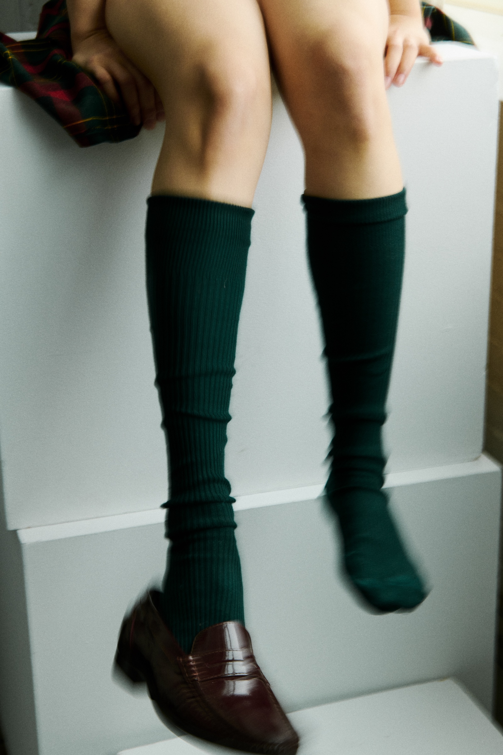 A seated student’s legs in green socks, one brown shoe resting nearby.